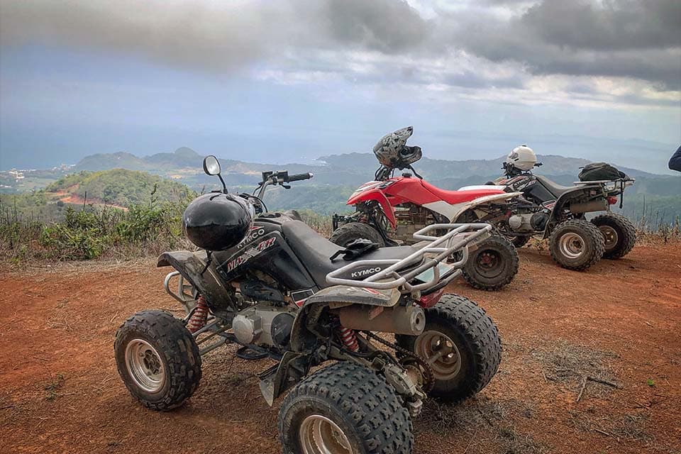 Three quads parked on a red-dirt ridge, the Pacific and the coastline laid out below.