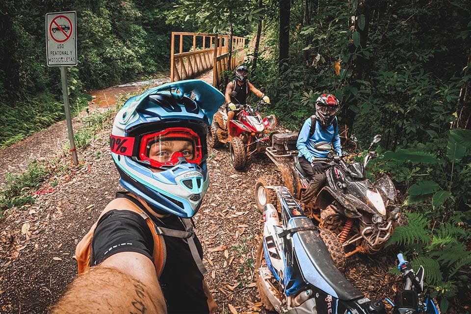 A helmet-cam view back down the line of quads stopped at a wooden bridge in the forest.