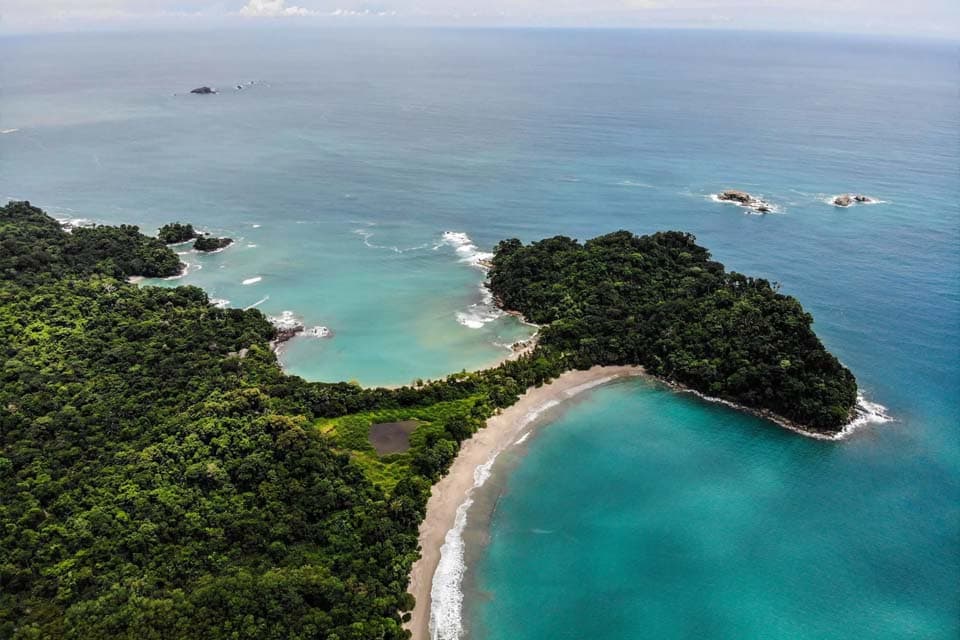 The park from the air: two bays either side of a forested point, reefs showing through turquoise water.