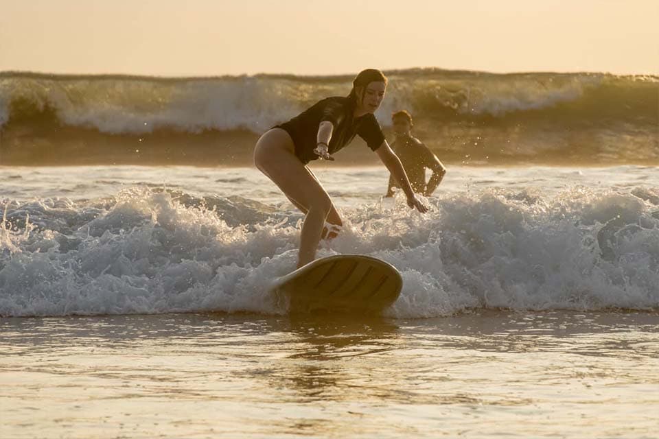 A student riding in at sunset, an instructor jogging alongside through the shallows.
