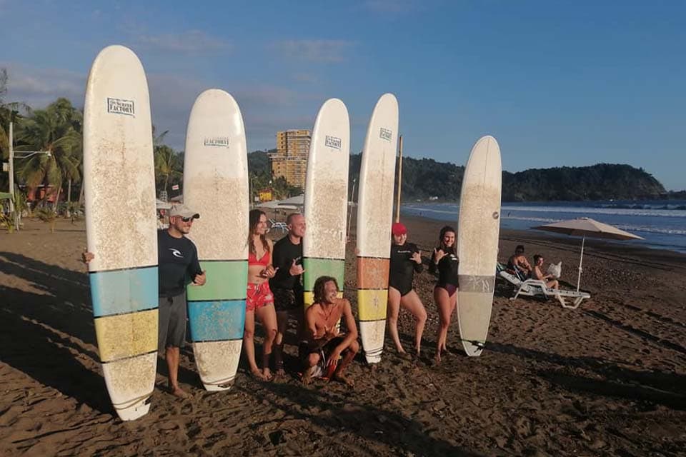 Six longboards stood upright in the sand at the end of a lesson, the students behind them and the headland beyond.