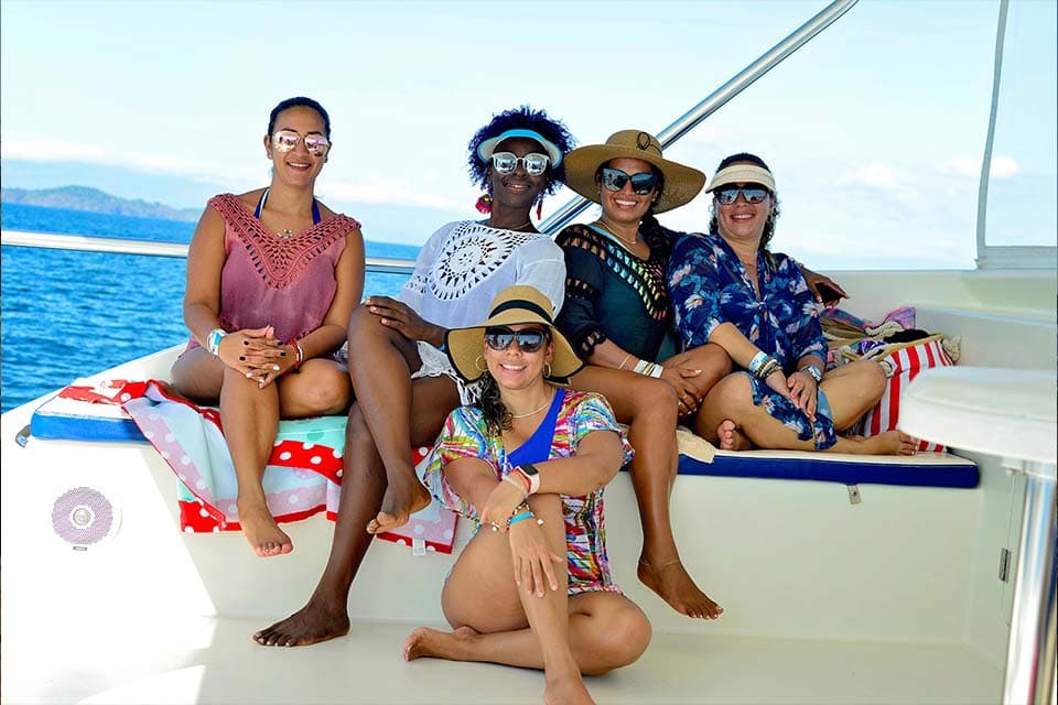 Guests sitting along the foredeck cushions in the shade, the gulf flat behind them.