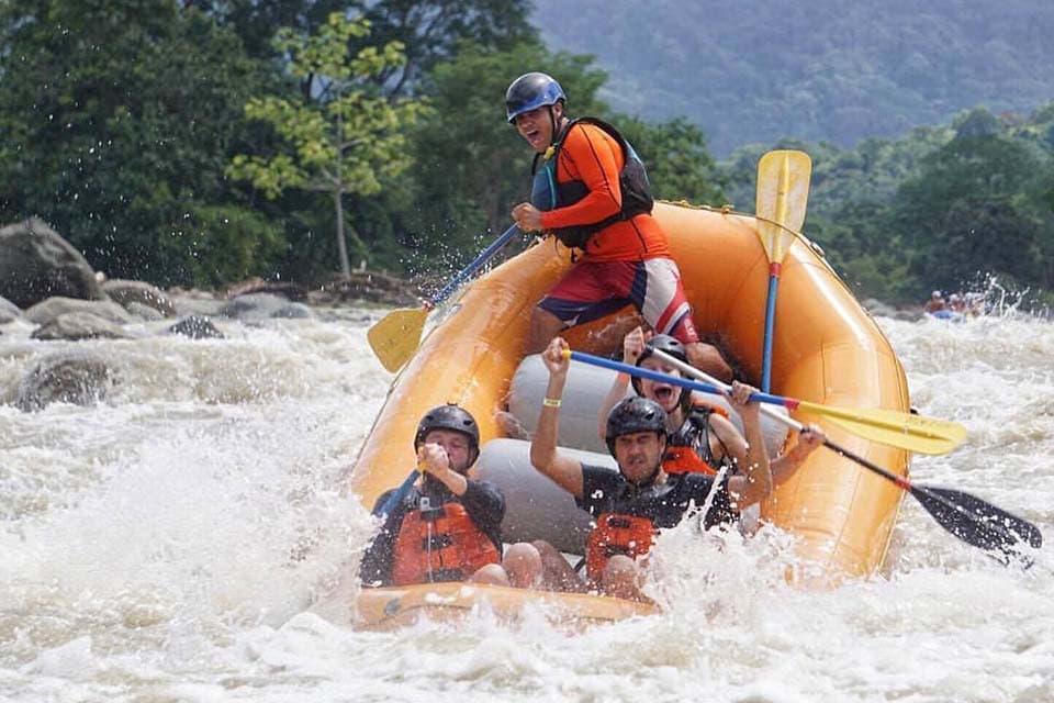 A raft punching through a standing wave, the guide up on the stern tube and spray over the bow.