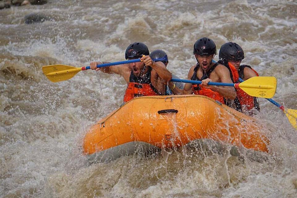 Four paddlers digging in as the raft buries its nose in whitewater.