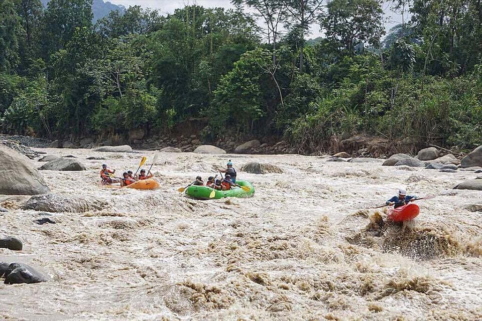 Three boats working down a wide brown rapid with forest on both banks.