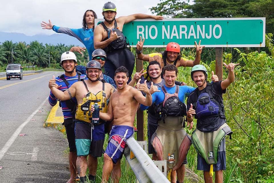 Guides and paddlers grouped under the Río Naranjo road sign, paddles and helmets up.